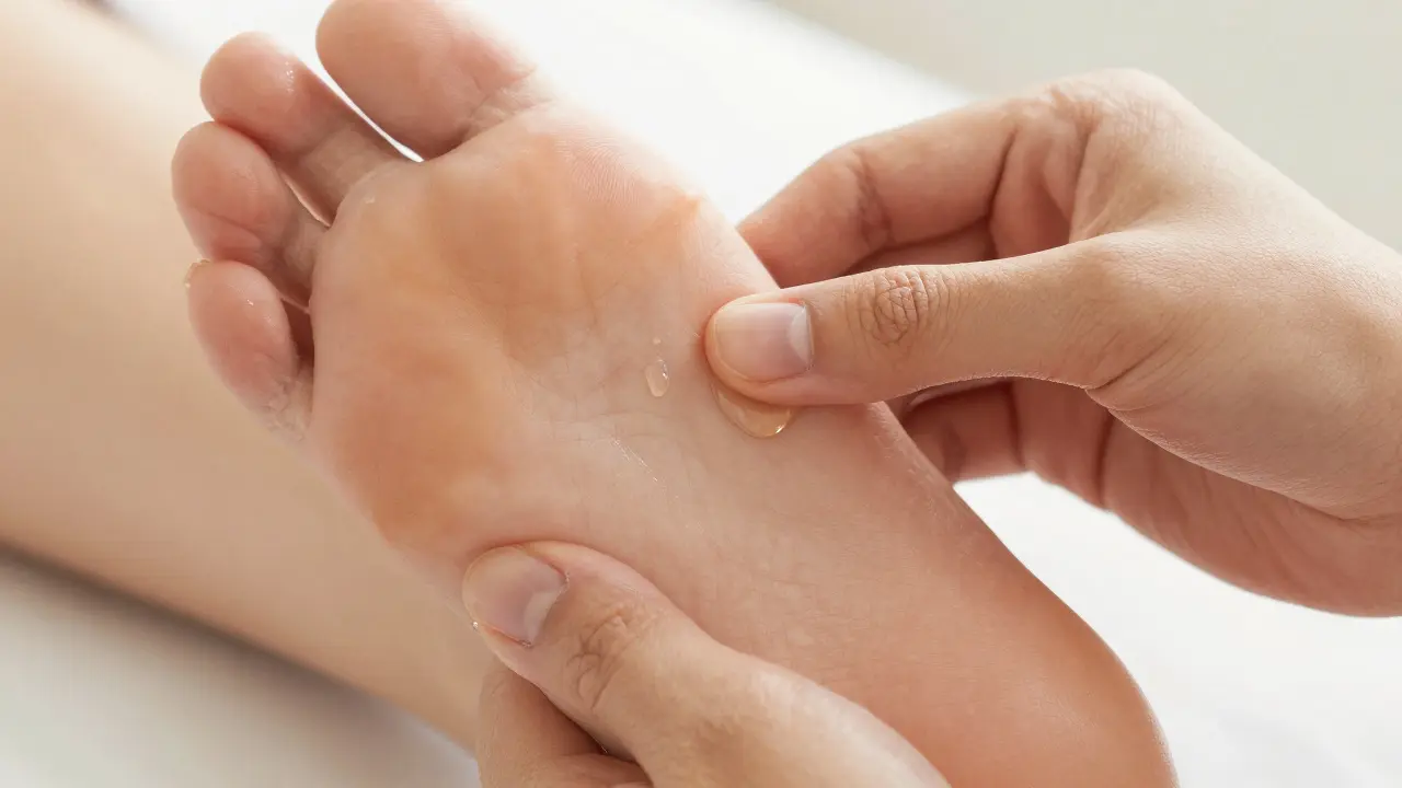 Detail ruky provádějící reflexní masáž vnějšího okraje plosky nohy s masážním olejem.